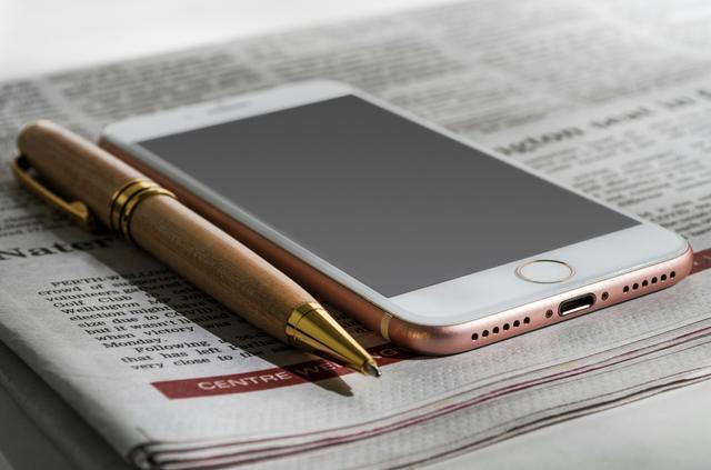 An iPhone and a pen resting on a newspaper.